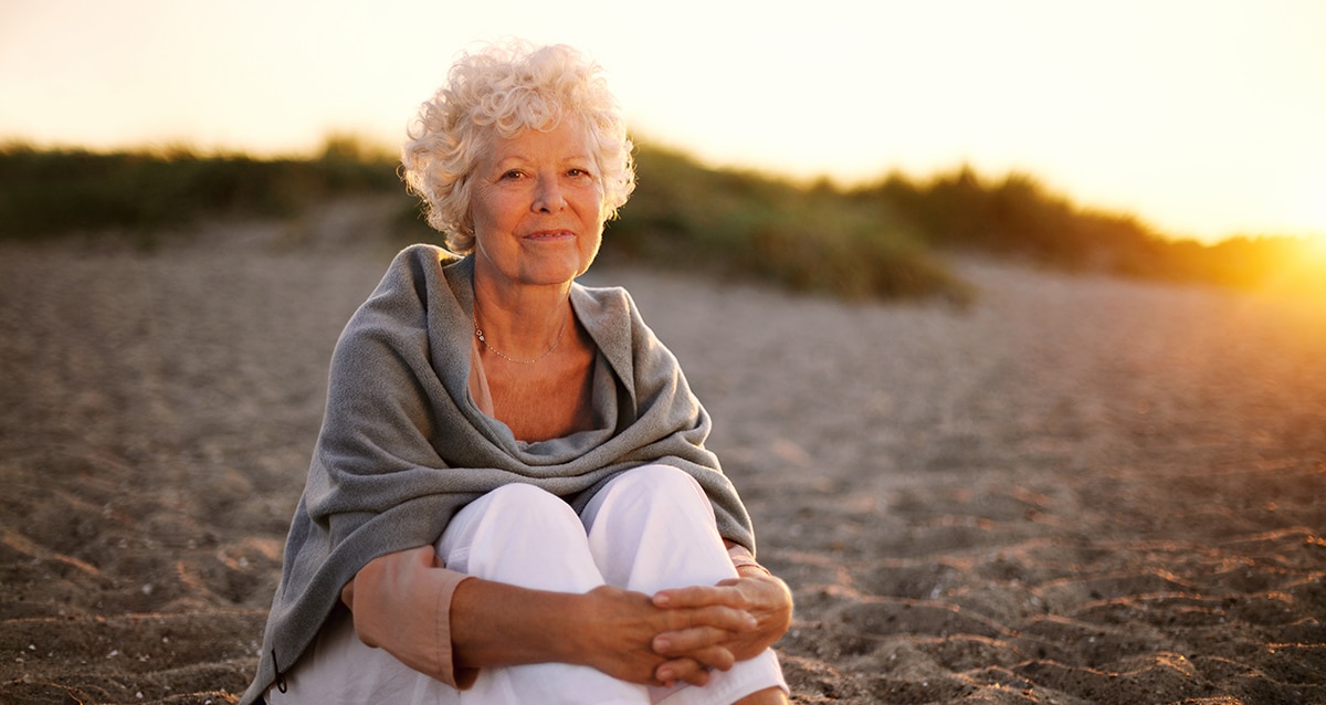 femme sénior cheveux blanc, semble calme et sereine. assise sur une plage couché de soleil. Plus d'ainés touchés par l'endettement